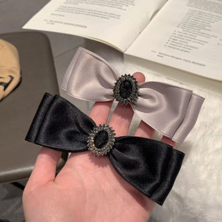 Black and silver hair bow held in a hand with an open book in the background