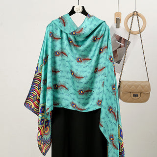 Turquoise scarf with peacock feather pattern draped over a black garment, next to a beige handbag on a white background.