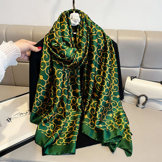 Green and gold patterned scarf draped over a black jacket on a light gray couch.