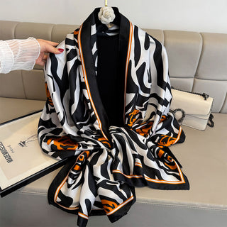 Black, white, and orange patterned scarf draped over a sofa with a hand holding it.