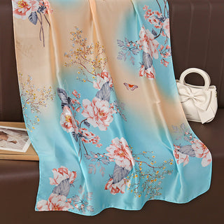 Floral scarf with a gradient background on a brown surface with a white handbag.