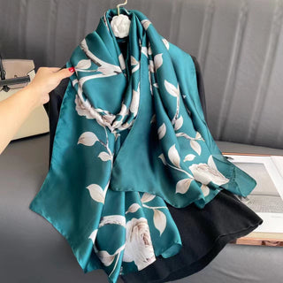 Teal scarf with floral pattern held by a hand against a neutral background