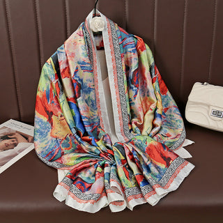 Colorful scarf with artistic design draped over a surface, with a magazine and white bag in the background.
