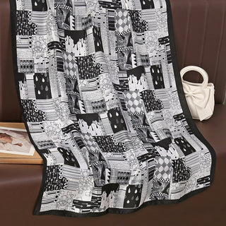 Black and white patchwork blanket on a brown surface with a white handbag and photo frame.