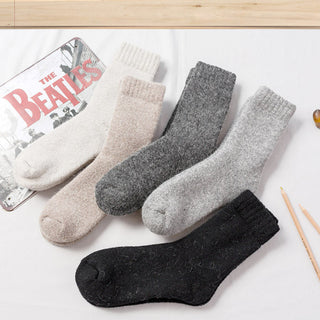 Three pairs of socks in gray, beige, and black on a white surface with a Beatles album cover in the background.