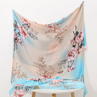 Floral scarf with pink flowers and blue sky draped over a chair on a white background