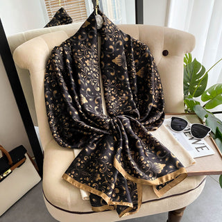 Black and gold patterned scarf draped over a beige chair with a plant and magazine in the background.