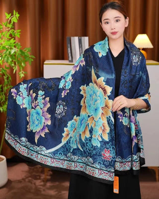Woman holding a large floral-patterned blue scarf in a room with a lamp and plant.