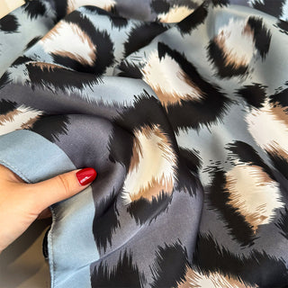 Fabric with a leopard print pattern held by a hand with red nail polish.